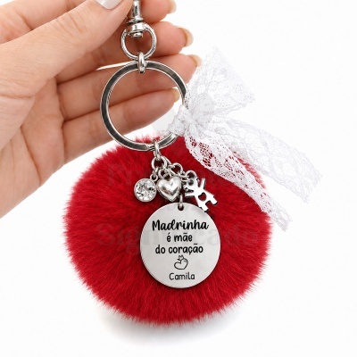 Porta-chaves com pompom vermelho e pendente metálico com escrita em português.