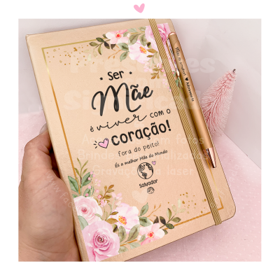 Caderno bege claro com flores e texto sobre ser mãe, com caneta dourada presa a elástico
