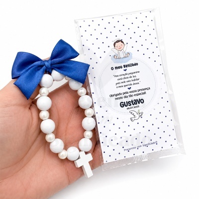 Pulseira branca com laço azul e cartão de batizado com texto e desenho de anjo