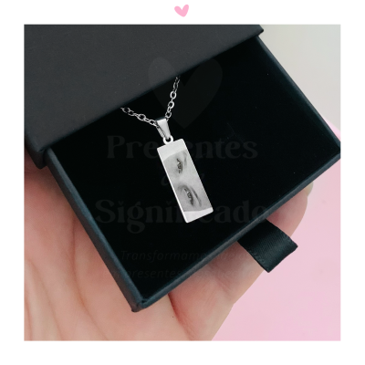 Colar prateado com pendente retangular dentro de caixa preta