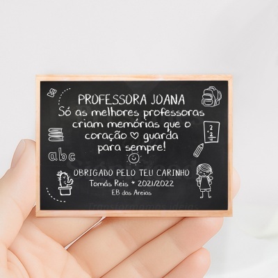 Mini quadro negro com texto e desenhos escolares em branco, segurado por uma mão.