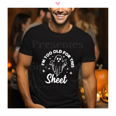 Homem sorridente com camisola preta estampada de fantasma e texto humorístico, cenário com abóboras.