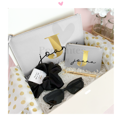 Conjunto de carteira e porta-moedas cinzas com letra J e nome, elástico de cabelo preto, óculos de sol e caneta dourada numa caixa decorativa