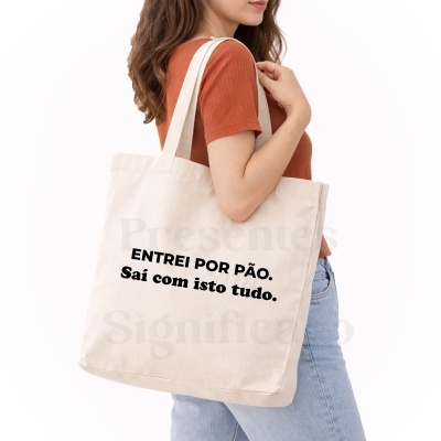 Mulher a usar saco de tecido crú com texto preto ENTREI POR PÃO. Sai com isto tudo.