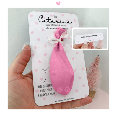 Balão rosa amarrado num cartão branco decorado com corações rosas e texto em português.