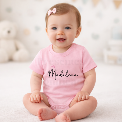 Bebé com body cor-de-rosa e texto Madalena sentado em espaço interior claro