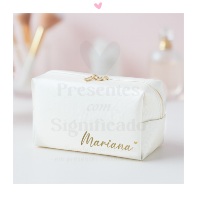 Necessaire branca com fecho dourado e nome Maria em dourado, sobre fundo rosa com pincéis e frasco desfocados