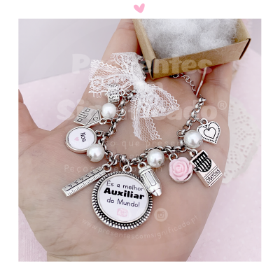 Pulseira prateada com pingentes variados e mensagem 'És a melhor Auxiliar do Mundo!' com laço de renda