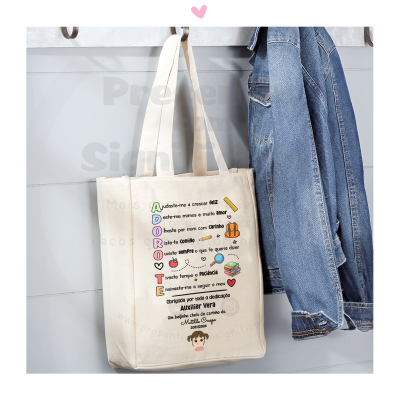 Saco de tecido bege com texto colorido sobre acróstico pendurado na parede junto a casaco de ganga azul