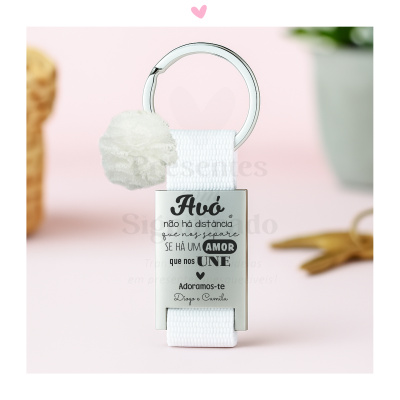 Chaveiro branco com argola metálica e placa gravada com mensagem para avó, fundo rosa claro.