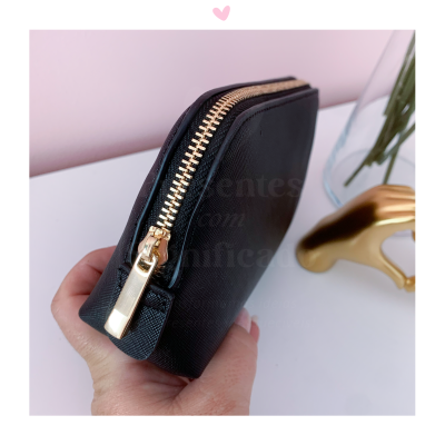 Carteira preta com fecho dourado numa mão sobre mesa branca e fundo rosa