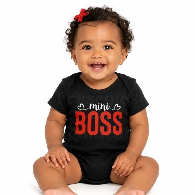 Bebé sorridente com body preto com texto mini BOSS e laço vermelho no cabelo.