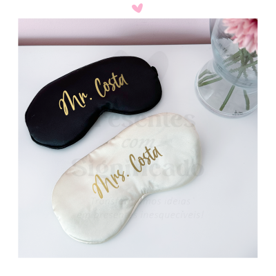 Máscaras de dormir preta e branca com inscrições em dourado Mr. Costa e Mrs. Costa ao lado de vaso com flores