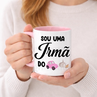 Caneca branca com interior e pega rosa com texto em preto e ilustrações, segurada por mulher de suéter bege.