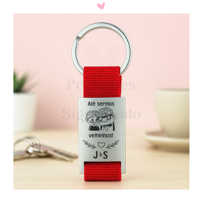 Porta-chaves com fita vermelha e parte metálica gravada com texto e ilustração de casal idoso