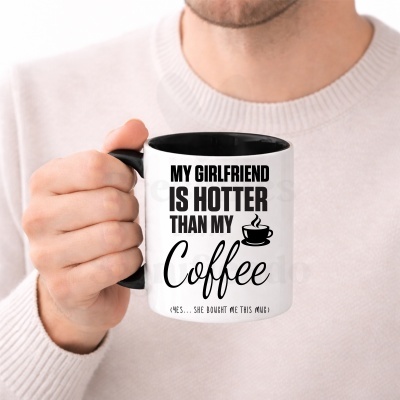 Caneca branca com pega preta e texto em inglês MY GIRLFRIEND IS HOTTER THAN MY Coffee segurada por uma mão