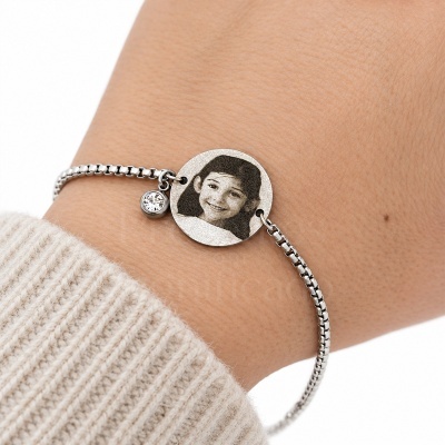 Pulseira prateada com pendente redondo gravado com foto e pendente com pedra brilhante no pulso.