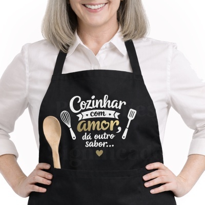 Avental preto com texto e ilustrações de utensílios de cozinha, usado por pessoa com camisa branca