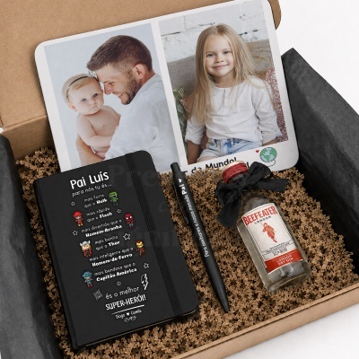 Caixa de oferta com caderno preto, caneta, mini garrafa de gin e cartão com fotos de crianças e adulto