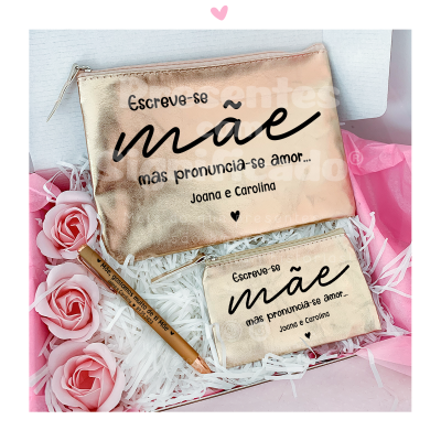 Carteira e carteira pequena douradas com texto em preto e caneta dourada num embrulho com papel branco e rosas cor-de-rosa