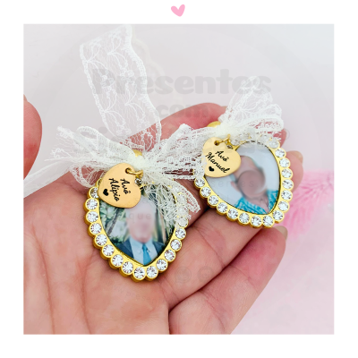 Duas molduras de coração douradas com pedras e laços de renda, cada uma com foto e pendente com nomes Avó Maria e Avô Manuel.