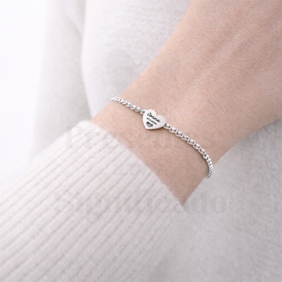 Pulseira prateada com pendente em forma de coração personalizado com nome e data no pulso.