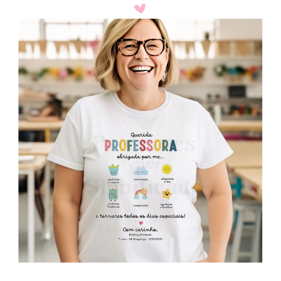 Camiseta branca com texto e desenhos infantis, usada por mulher sorridente numa sala de aula