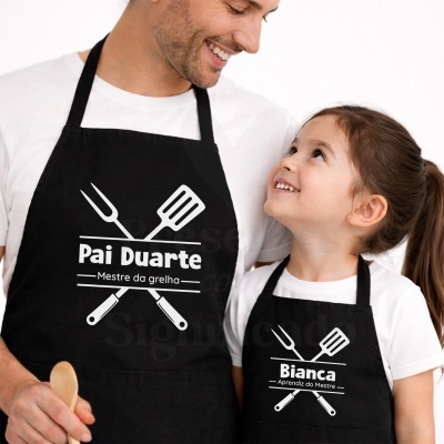 Aventais pretos com texto branco para pai e filha sobre grelha, homem e menina sorrindo em fundo branco.