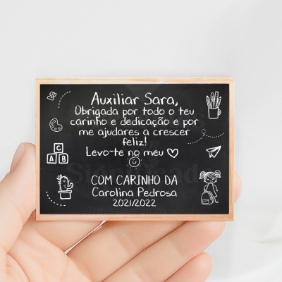 Pequeno quadro negro com moldura de madeira e texto em português branco e desenhos decorativos, segurado por mão.
