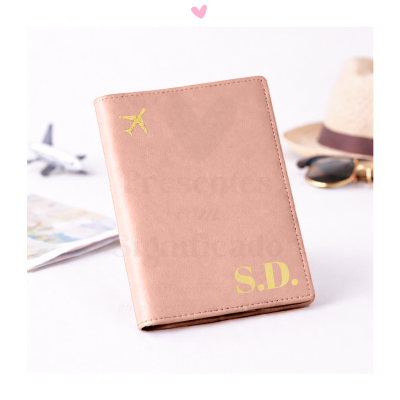 Capa de passaporte rosa com avião e iniciais douradas sobre superfície branca