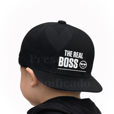 Boné preto com texto branco THE REAL BOSS e emoji usado por criança visto de trás.