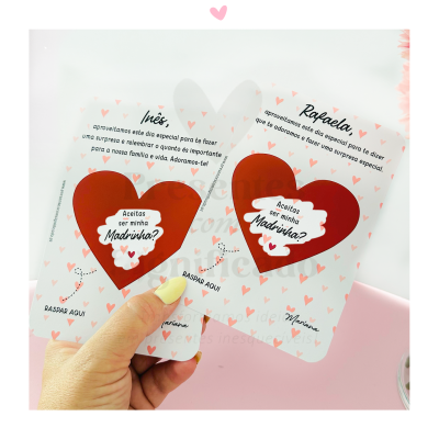 Cartas de convite para madrinha com corações vermelhos e textos impressos, numa mão sobre mesa rosa