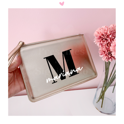 Carteira dourada com letra M e nome mariana segurada junto a vaso com flores rosa