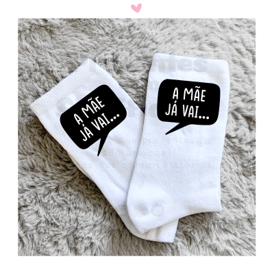 Par de meias brancas com texto 'A MÃE JÁ VAI...' em balão de fala preto