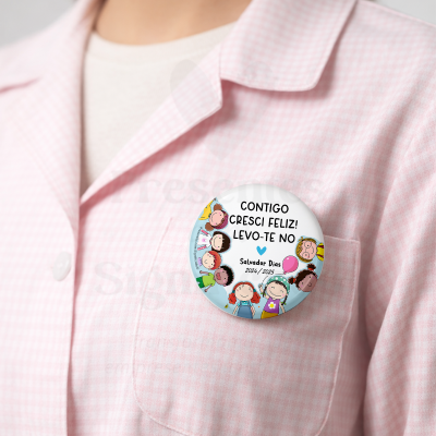 Botão redondo ilustrado com crianças e texto em português, preso em camisa rosa