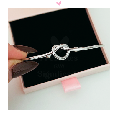 Pulseira prateada com nó sobre caixa rosa