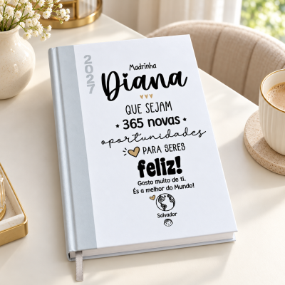 Caderno branco com texto personalizado para madrinha Diana junto a caneca de café e flores num ambiente claro