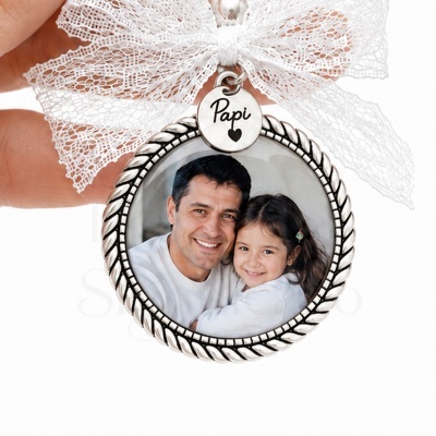 Medalhão prateado redondo com foto de homem e menina, laço de renda branca e pendente com texto Papi