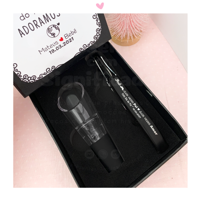 Caixa preta com soprador de nariz translúcido preto e caneta preta com texto branco, em superfície rosa com padrão de bolinhas