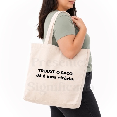 Mulher com camiseta verde a usar saco de tecido bege claro com texto preto impresso.