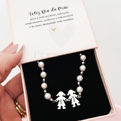 Colar com pérolas e pendentes metálicos com figuras femininas numa caixa rosa com cartão de Dia da Mãe