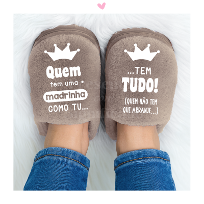 Chinelos castanhos com texto branco para madrinha, usados por pessoa de jeans sobre tapete branco.