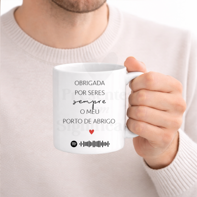 Caneca branca com texto em preto e vermelho numa mão.