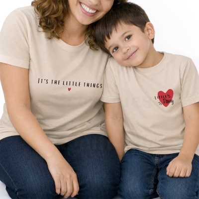 Duas pessoas com t-shirts bege estampadas com texto e corações vermelhos, sentados, fundo branco.