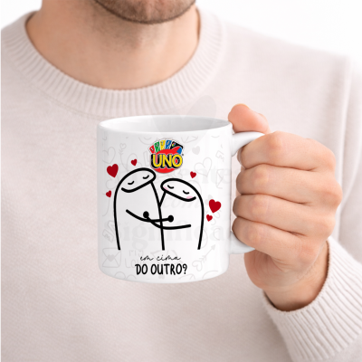 Caneca branca com ilustração de dois bonecos a abraçar e texto em português, segurada por uma mão masculina.