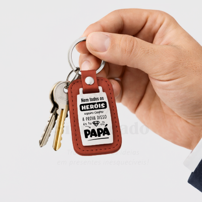 Chaveiro de couro castanho com texto em português sobre heróis e papá em fundo branco