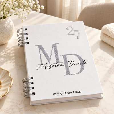 Caderno branco com texto personalizado numa mesa com vaso de flores e toalha