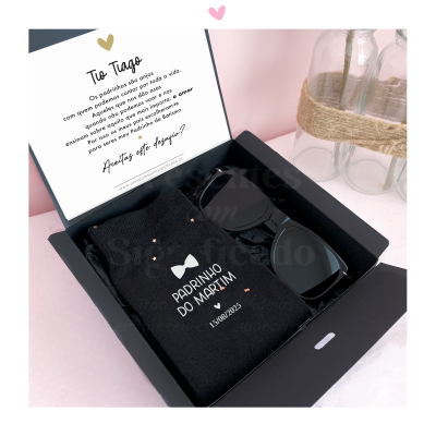 Caixa de presente preta com meias e óculos de sol em fundo rosa