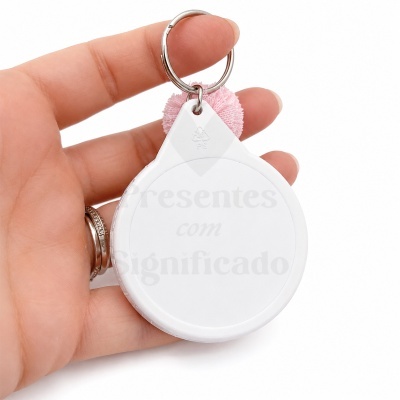Chaveiro branco circular com pompom rosa e argola sendo segurado por uma mão