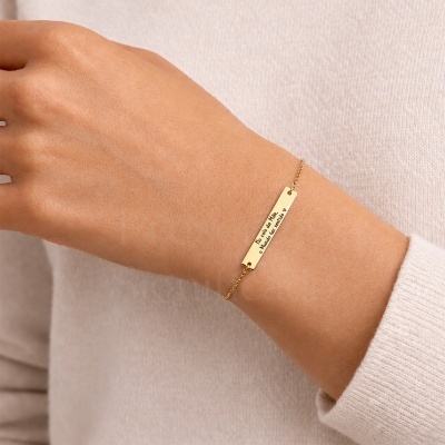 Pulseira dourada fina com placa gravada usada num pulso